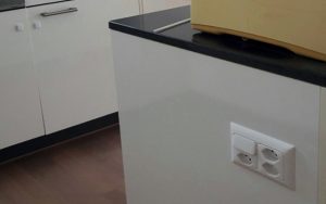 3 prises de courant installées à côté d'un interrupteur, sur le côté de l'ilot central dans une cuisine en Suisse